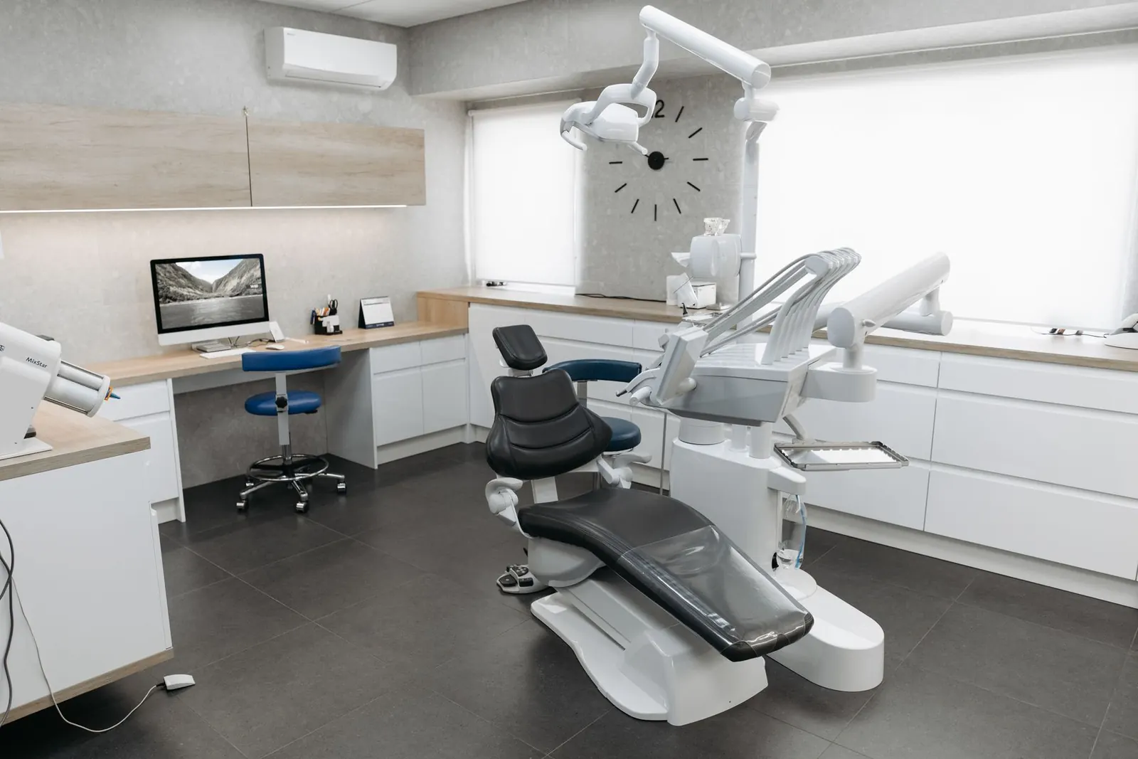 A bright, calm treatment room: an empty dental chair, tidy white cabinetry, and instruments resting in place